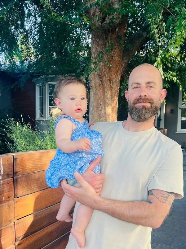Ido Grinberg holding his daughter outdoors, showcasing a meaningful family moment, representing personal transformation and life coaching
